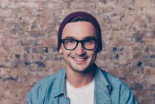 Man with glasses and knit hat in front of brick wall