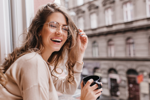 Smiling young woman wearing glasses and leaning out of window